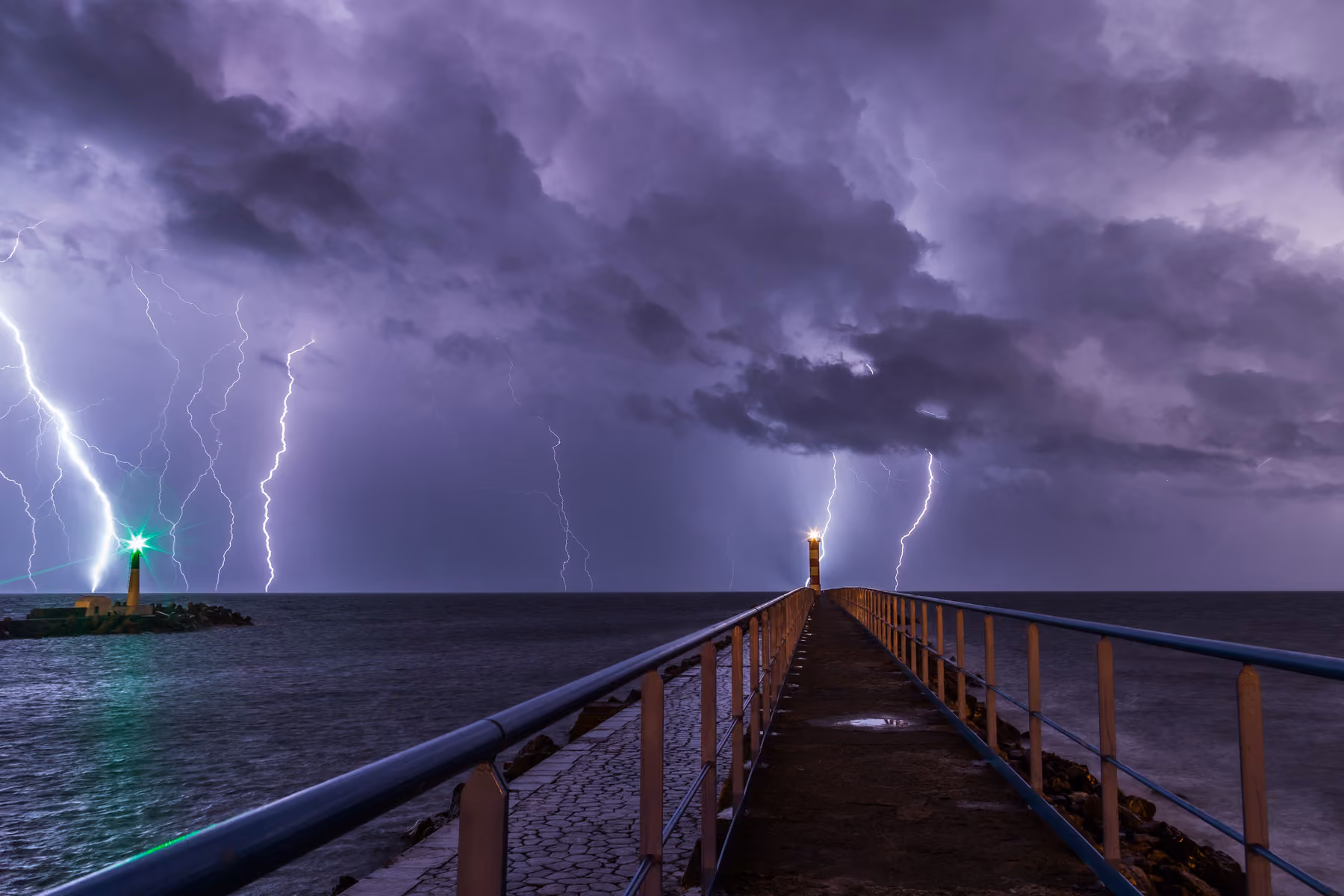 Lightning over a harbour breakwater with a lighthouse at its end